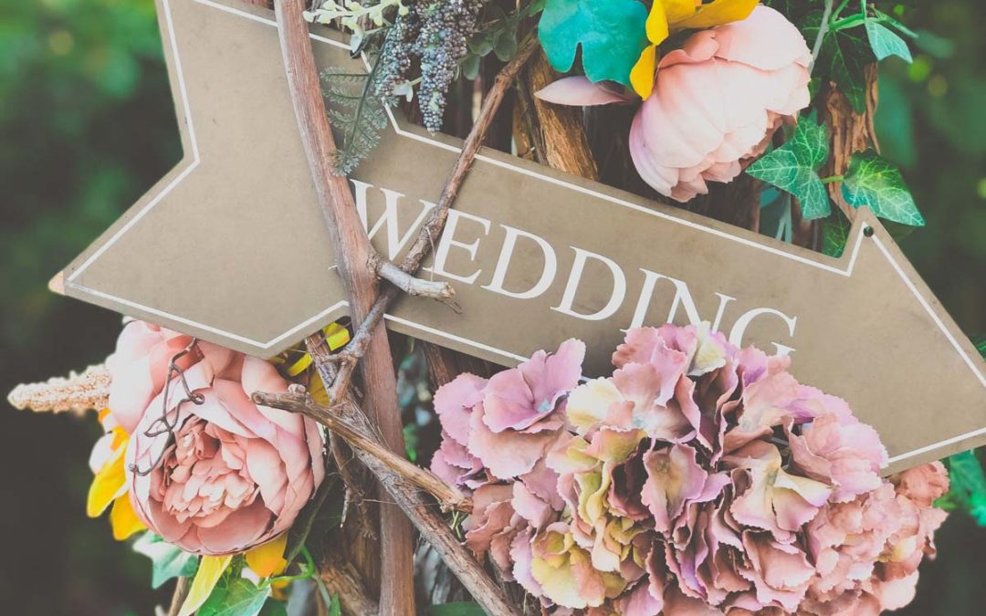 wedding sign shaped like an arrow on a post with flowers